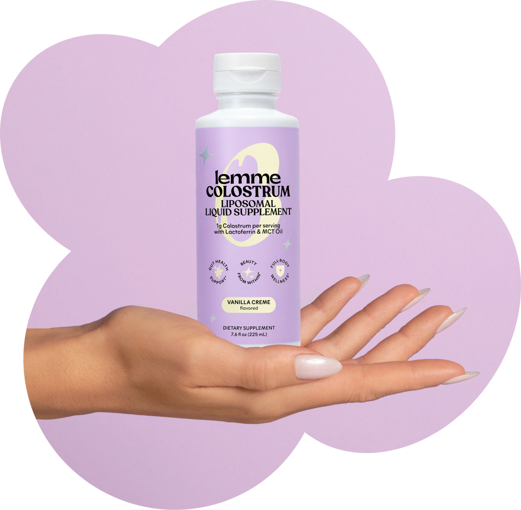 Hand holding a bottle of lemme colostrum supplement against a purple heart-shaped background