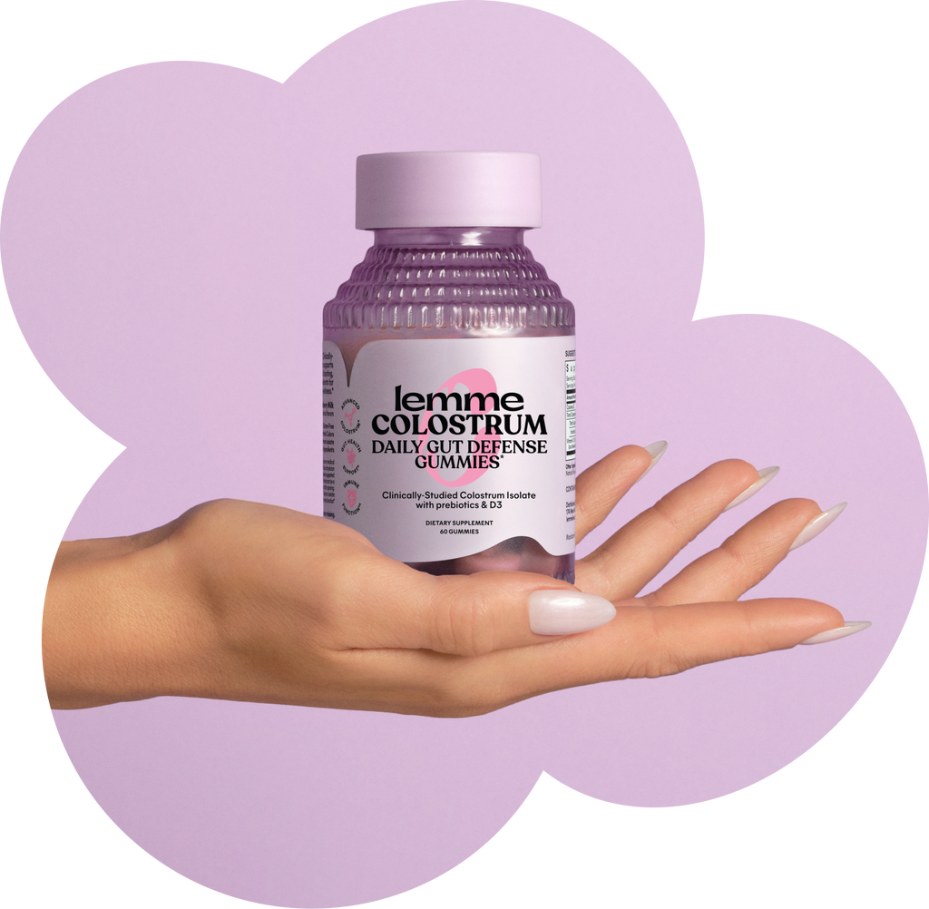 Hand holding a bottle of 'lemme colostrum' gummies against a purple heart-shaped background